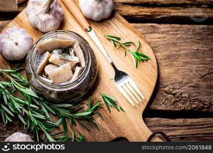 Pieces of salted herring in a glass jar on a cutting board. On a wooden background. High quality photo. Pieces of salted herring in a glass jar on a cutting board.