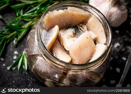Pieces of salted herring in a jar with rosemary and lemon. On a black background. High quality photo. Pieces of salted herring in a jar with rosemary and lemon.