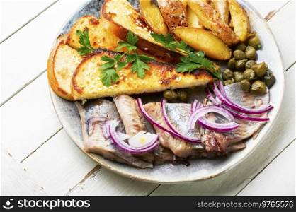 Pieces of salted herring with baked potatoes and toast.. Pieces of salted herring fish in a plate
