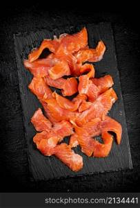 Pieces of salted salmon on a stone board. On a black background. High quality photo. Pieces of salted salmon on a stone board.