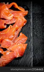 Pieces of salted salmon on a stone board. On a black background. High quality photo. Pieces of salted salmon on a stone board.