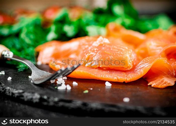 Pieces of salted salmon on a stone board with greenery. Macro background. High quality photo. Pieces of salted salmon on a stone board with greenery.