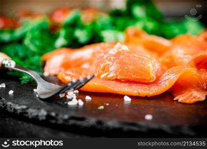 Pieces of salted salmon on a stone board with greenery. Macro background. High quality photo. Pieces of salted salmon on a stone board with greenery.