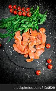 Pieces of salted salmon with greenery on a stone board. On a black background. High quality photo. Pieces of salted salmon with greenery on a stone board.