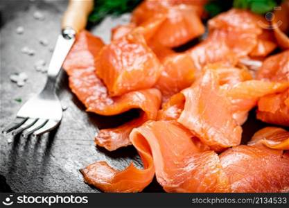 Pieces of salted salmon with greenery on a stone board. On a black background. High quality photo. Pieces of salted salmon with greenery on a stone board.