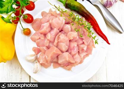 Pieces of sliced chicken breast with garlic, hot pepper and thyme in a plate, napkin, parsley and vegetables on a wooden plank background