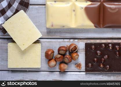 pieces of tile chocolates, nuts and cocoa beans on wooden background