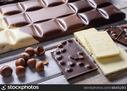 pieces of tile chocolates, nuts and cocoa beans on wooden background