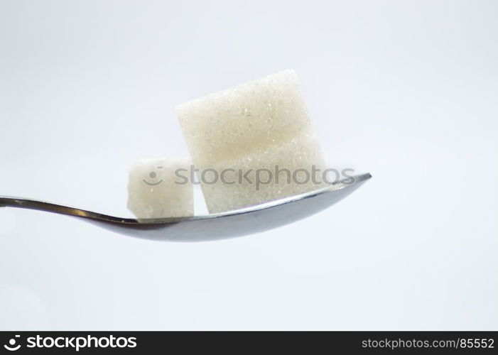 Pieces of white sugar on a stainless . Pieces of white sugar on a stainless steel spoon on a white background