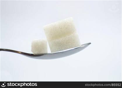Pieces of white sugar on a stainless . Pieces of white sugar on a stainless steel spoon on a white background