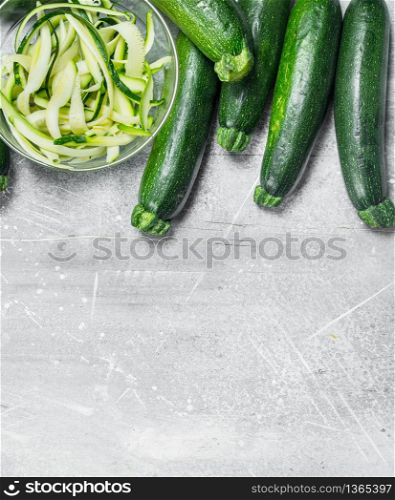 Pieces of zucchini in a bowl and a fresh whole zucchini. On white rustic background. Pieces of zucchini in a bowl and a fresh whole zucchini.