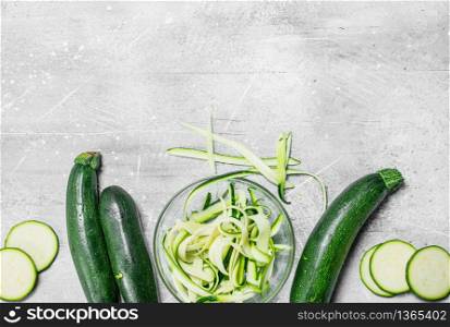Pieces of zucchini in a bowl and a fresh whole zucchini. On white rustic background. Pieces of zucchini in a bowl and a fresh whole zucchini.