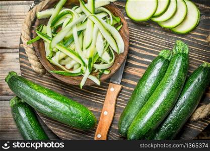 Pieces of zucchini in a bowl on a cutting Board with a knife. On wooden background. Pieces of zucchini in a bowl on a cutting Board with a knife.