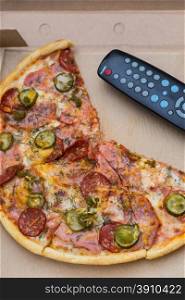 pieces pizza with sausages and bacon in pasteboard box with tv remote control