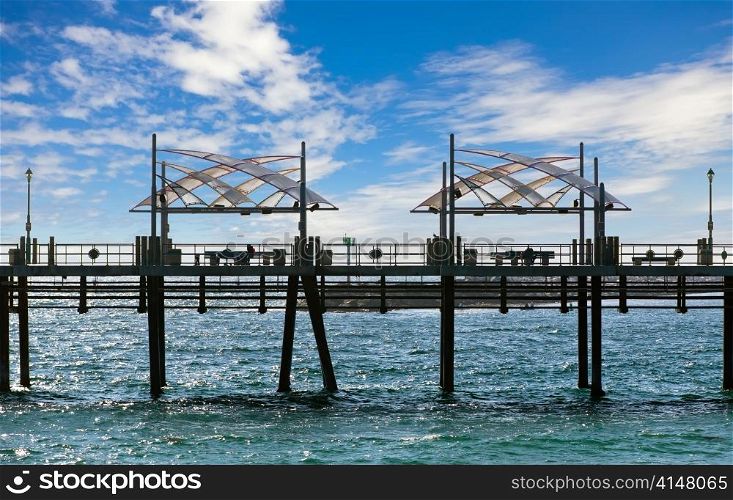 Pier with benches and lanterns above the ocean and blue sky with clouds