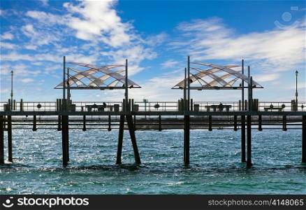 Pier with benches and lanterns above the ocean and blue sky with clouds