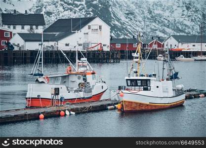Pier with ships in Hamnoy fishing village on Lofoten Islands, Norway with red rorbu houses in winter. Hamnoy fishing village on Lofoten Islands, Norway