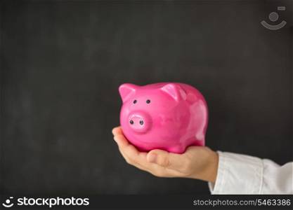 Piggy bank in hand against blackboard blank