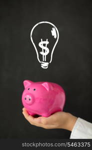 Piggy bank in hand against blackboard with drawing bulb lamp. Idea concept