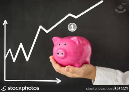 Piggy bank in hand against blackboard with growing chart