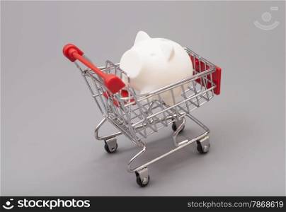 Piggy bank in shopping cart isolated on gray background