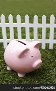Piggy Bank On Grass With White Fence