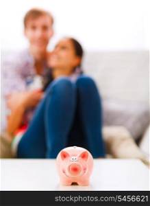 Piggy bank on table and happy young couple in background&#xA;