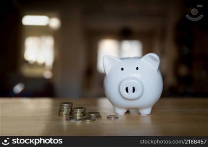 Piggy bank with stack coins on wooden table with blurry background of living room