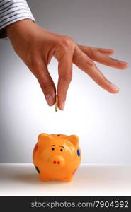 Piggybank and hand with coin.
