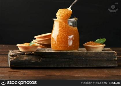 pike caviar in a glass jar and round tartlets on a black background, close up