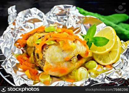 Pike with carrots, leek, basil and lemon slices in a foil on a metal grid, green towel on a dark wooden board