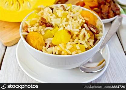 Pilaf fruit with pumpkin, raisins, dried apricots in a bowl on a saucer, pumpkin, dried fruit, napkin, spoon on a background of light wooden boards