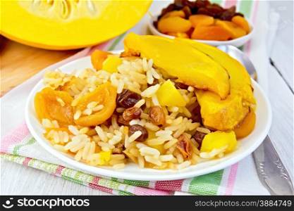 Pilaf fruit with pumpkin, raisins, dried apricots in a white plate on a napkin, pumpkin, dried fruits, spoon background of light wooden boards