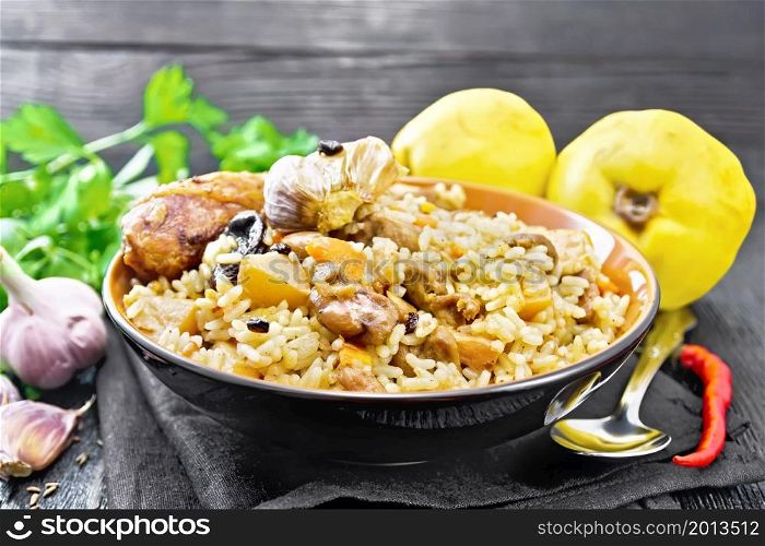 Pilaf of rice, duck, quince, carrots with garlic, onion, prunes and spices in a plate on a kitchen towel on wooden board background