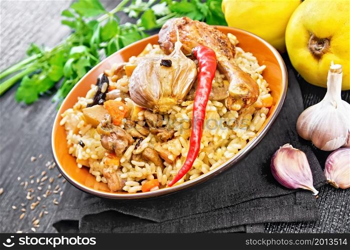 Pilaf of rice, duck, quince, carrots with garlic, onion, prunes and spices in a plate on a napkin on wooden board background