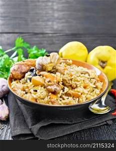 Pilaf of rice, duck, quince, carrots with garlic, onion, prunes and spices in a plate on a napkin on black wooden board background