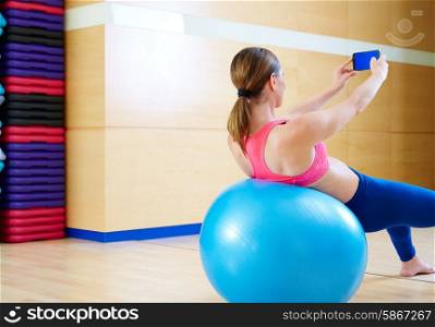 Pilates woman shoots selfie self portrait with mobile at gym relaxed with fitball