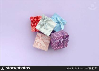 Pile of a small colored gift boxes with ribbons lies on a violet background. Minimalism flat lay top view.. Pile of a small colored gift boxes with ribbons lies on a violet background. Minimalism flat lay top view