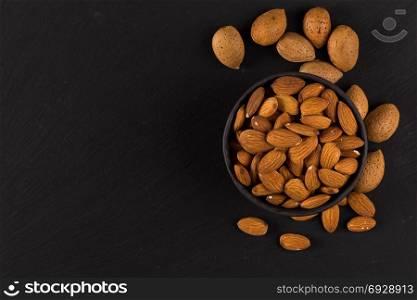 Pile of almonds nuts in a stone bowl on a dark black background