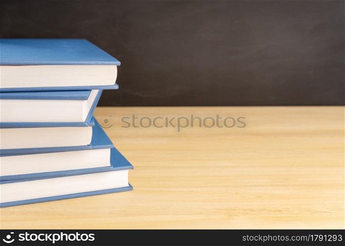 Pile of books on wooden table and black chalkboard at background with copy space. Back to school, education or learning concept