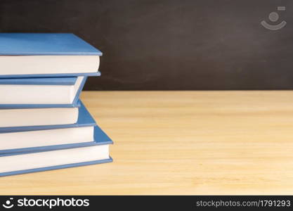 Pile of books on wooden table and black chalkboard at background with copy space. Back to school, education or learning concept