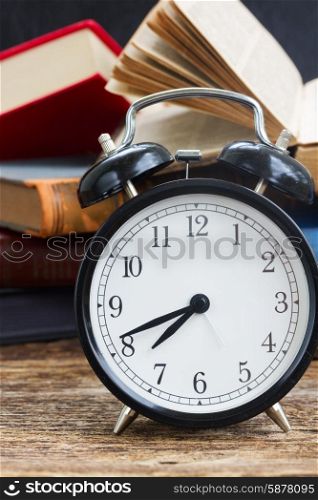 pile of books with clock. pile of old books with antique alarm clock on wooden shelf