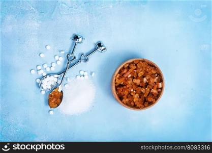 Pile of brown sugar cubes and stevia on blue wooden background