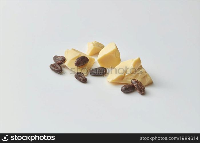 Pile of composed chunks of organic raw pure cocoa butter with brown bitter beans on gray background. Cocoa beans and butter chunks