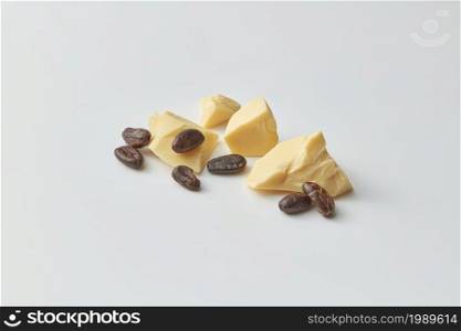 Pile of composed chunks of organic raw pure cocoa butter with brown bitter beans on gray background. Cocoa beans and butter chunks