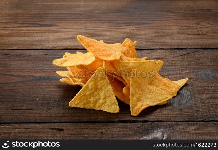 pile of corn tortilla chips or nachos on a brown wooden background, close up