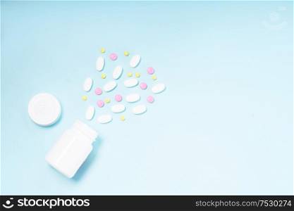Pile of falling colorful medical pills and bottle on blue background, top view. Pile of pills