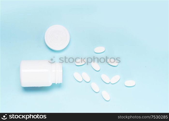 Pile of falling medical pills and white bottle on blue background, top view. Pile of pills