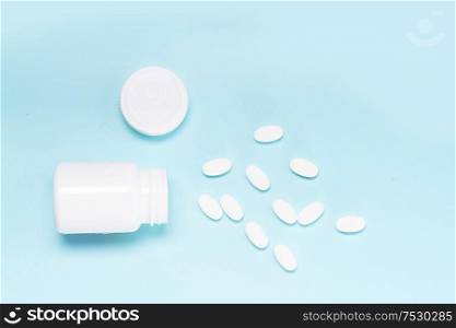 Pile of falling medical pills and white bottle on blue background, top view. Pile of pills
