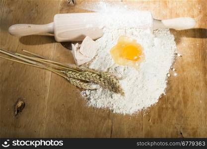 Pile of flour, rolling pin and wheat. Egg on flour